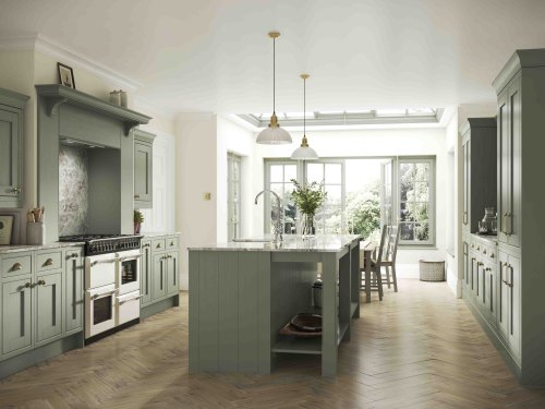this shows and example set of atlantic green kitchens. a light green shaker inframe kitchen is shown with a kitchen island and brass finish handles. The worktop is a marble effect and there are a selection of muted toned decor items
