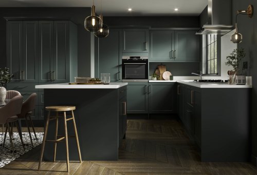 A Dark Green shaker Symphony kitchen with white worktops and dark wooden floors, along with wooden bar stools and brass handles and detailing such as lighting